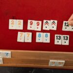 A hand arranging rummy tiles on a red felt table, ideal for leisure themes.