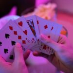 Vivid close-up of hands holding playing cards in a game setting with moody lighting.
